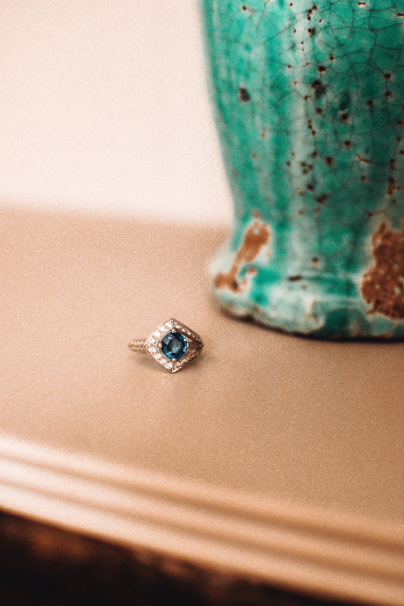 Foto eines Rings mit Diamanten und einem blauen Stein, daneben eine Vase